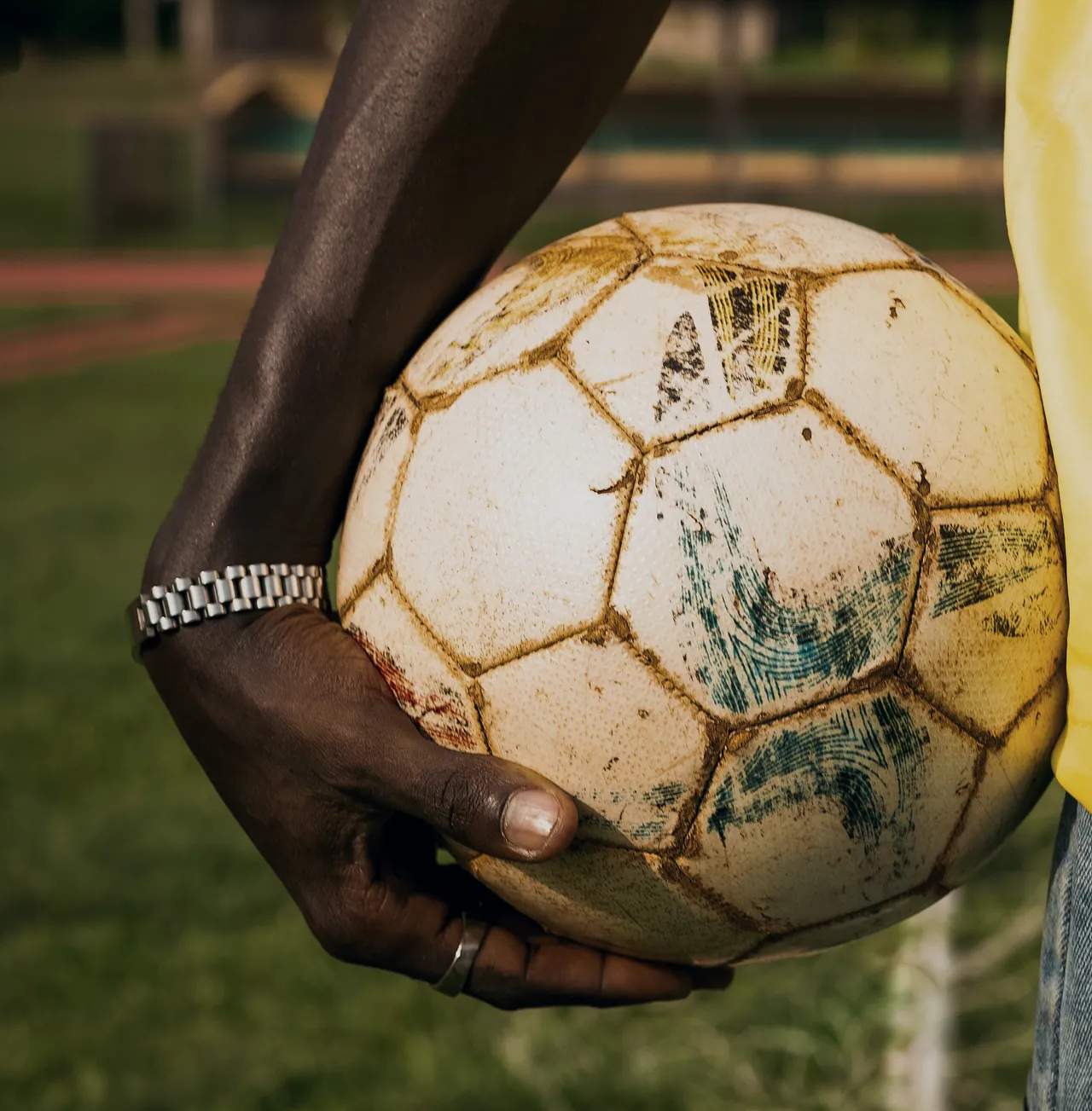 A hand holding a weathered leather match ball by the touchline.