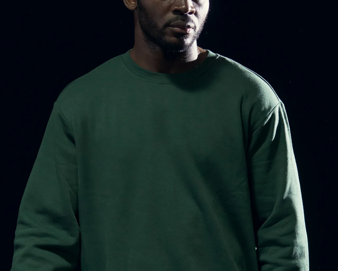 A player in a marsh-green crew-neck training sweat, shot against black.