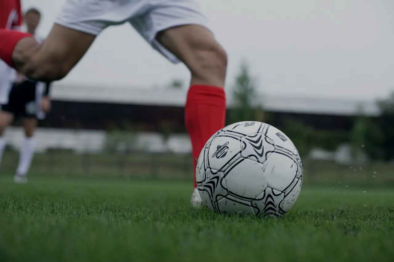 A white ball the instant before it is struck, low to the grass.