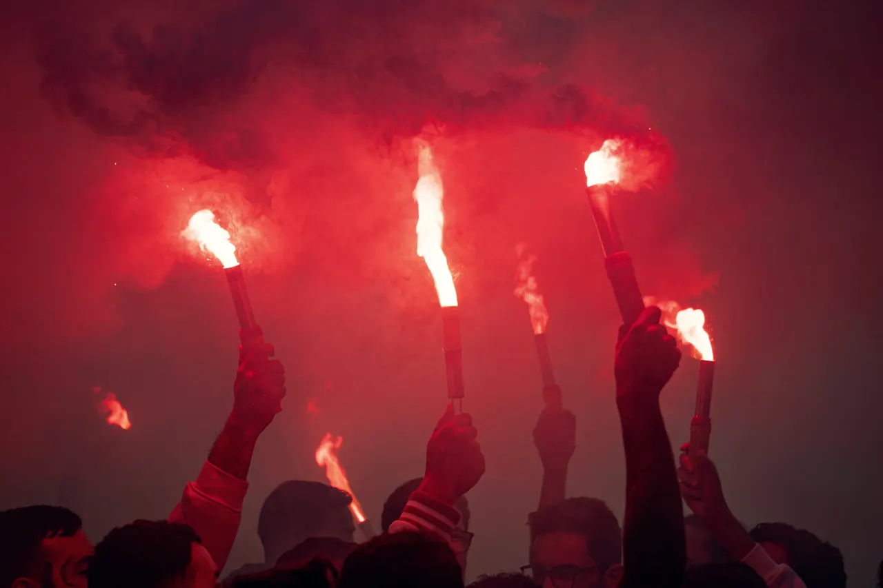 Red flares held high above a crowd, smoke filling the night.