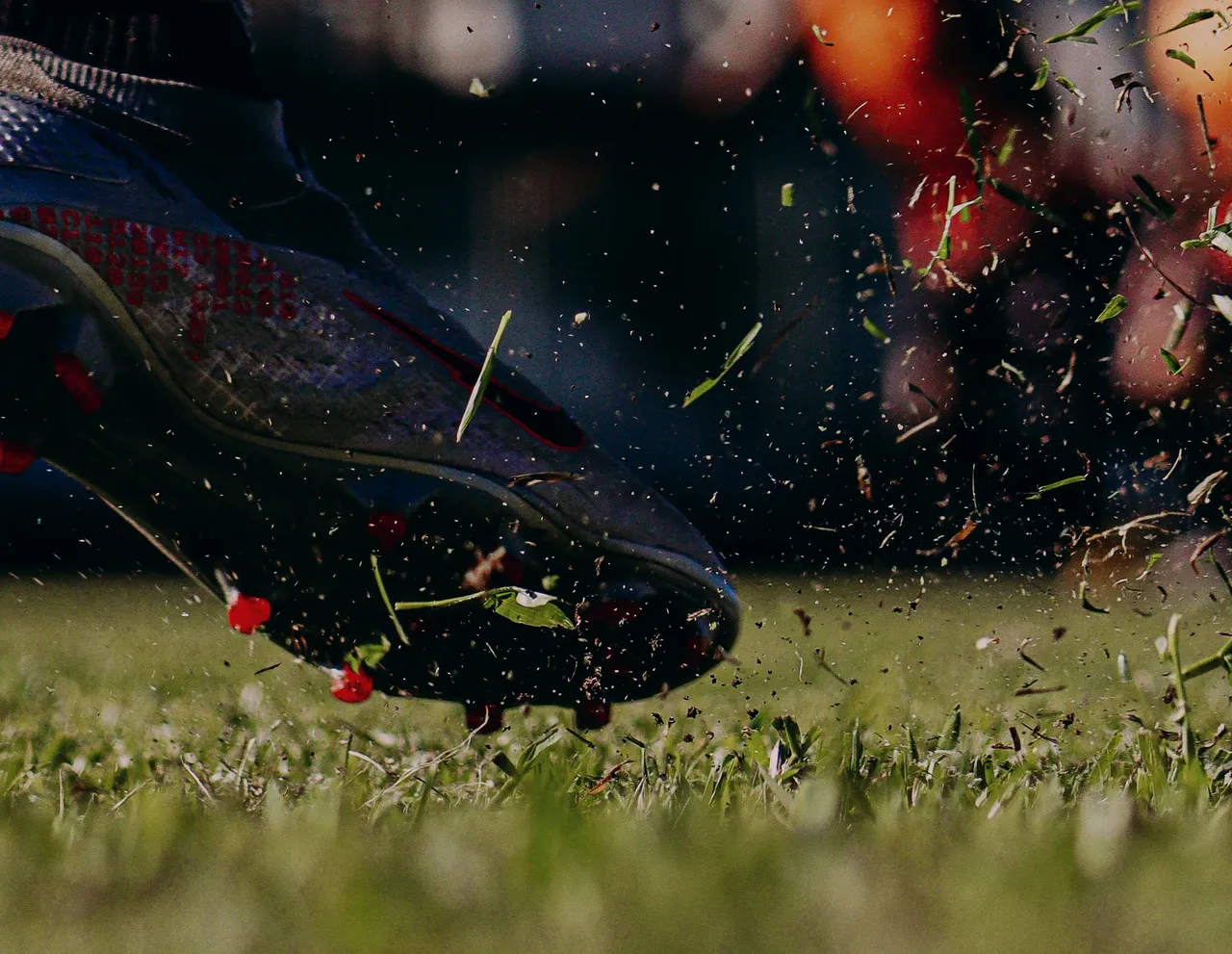 Close on the Night colourway: red-tipped studs biting into the turf as grass flies.