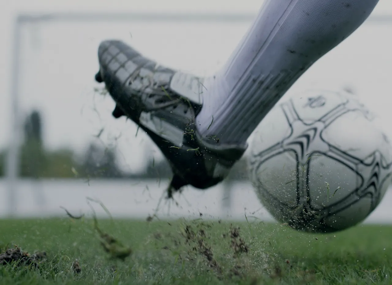 Close on a silver boot at the moment of contact, clods of turf in the air.