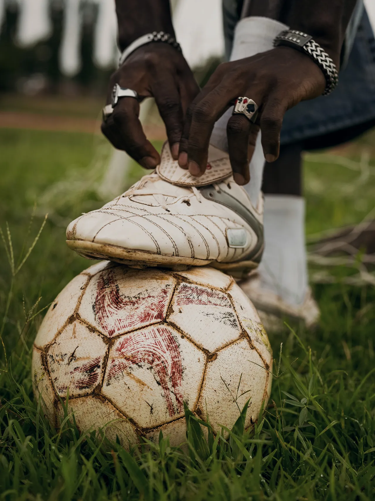 Hands pulling the laces tight on a worn white leather boot, the foot resting on an old ball.