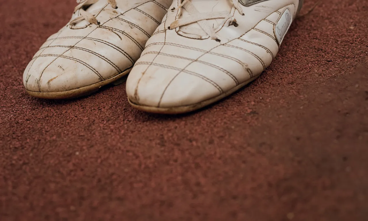 A pair of white leather boots side by side on a red running track.