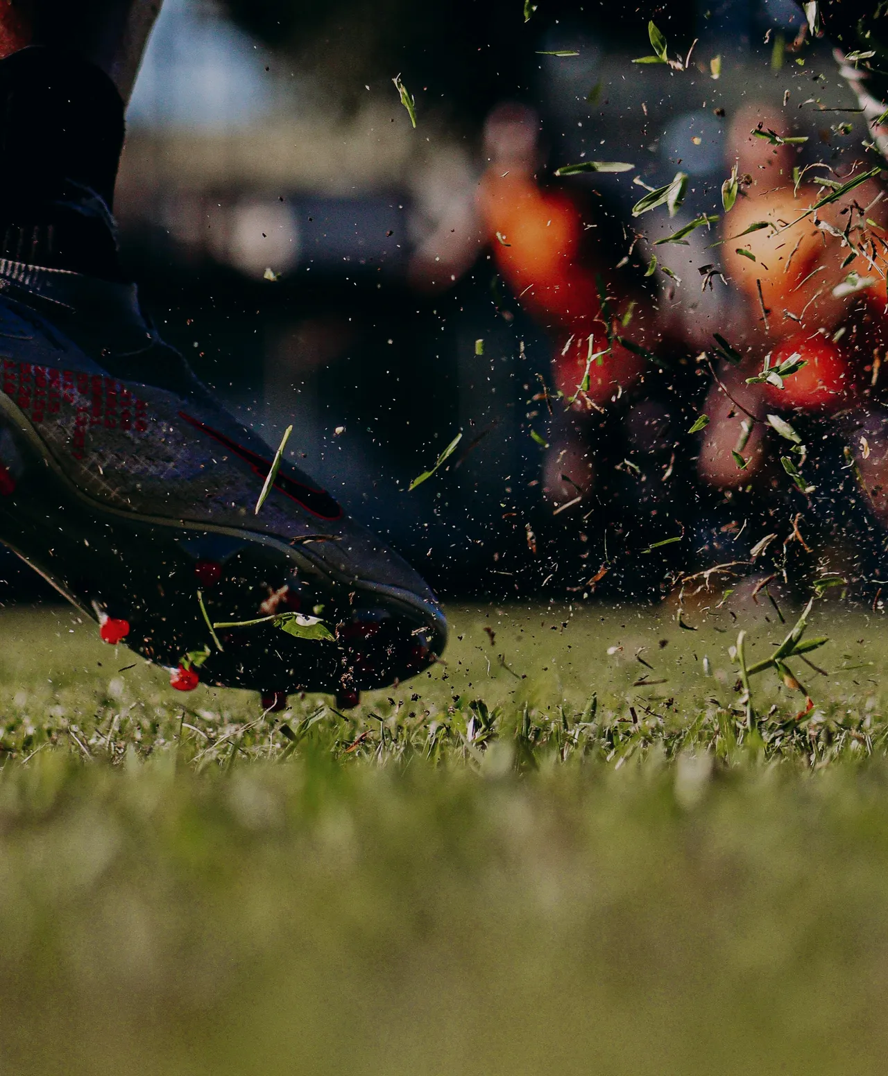 A boot strikes through the turf, sending blades of grass flying.