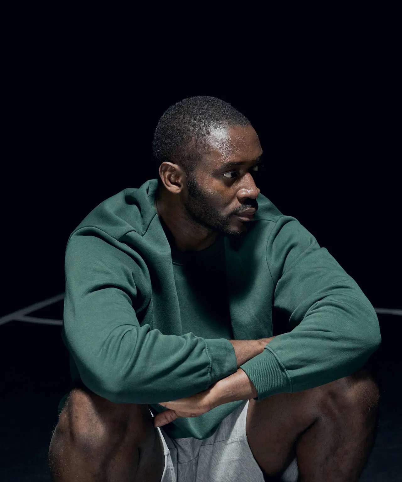 Ife Adeyemi crouched low in a green training sweat, staring past the camera.