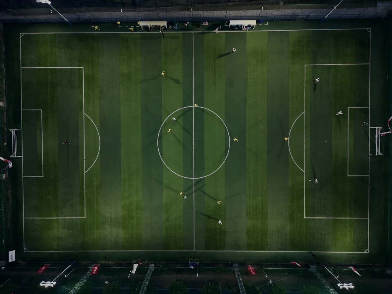 A full pitch seen from directly above, its markings sharp against striped grass.